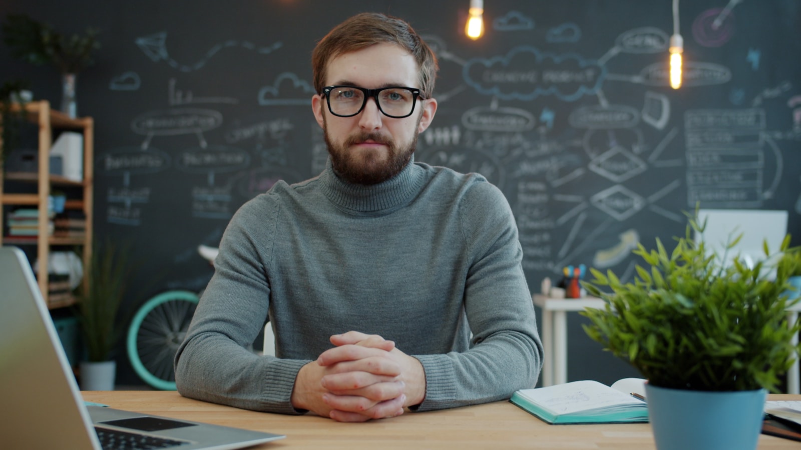 A business owner sits at a desk in front of a chalkboard covered in strategy diagrams.