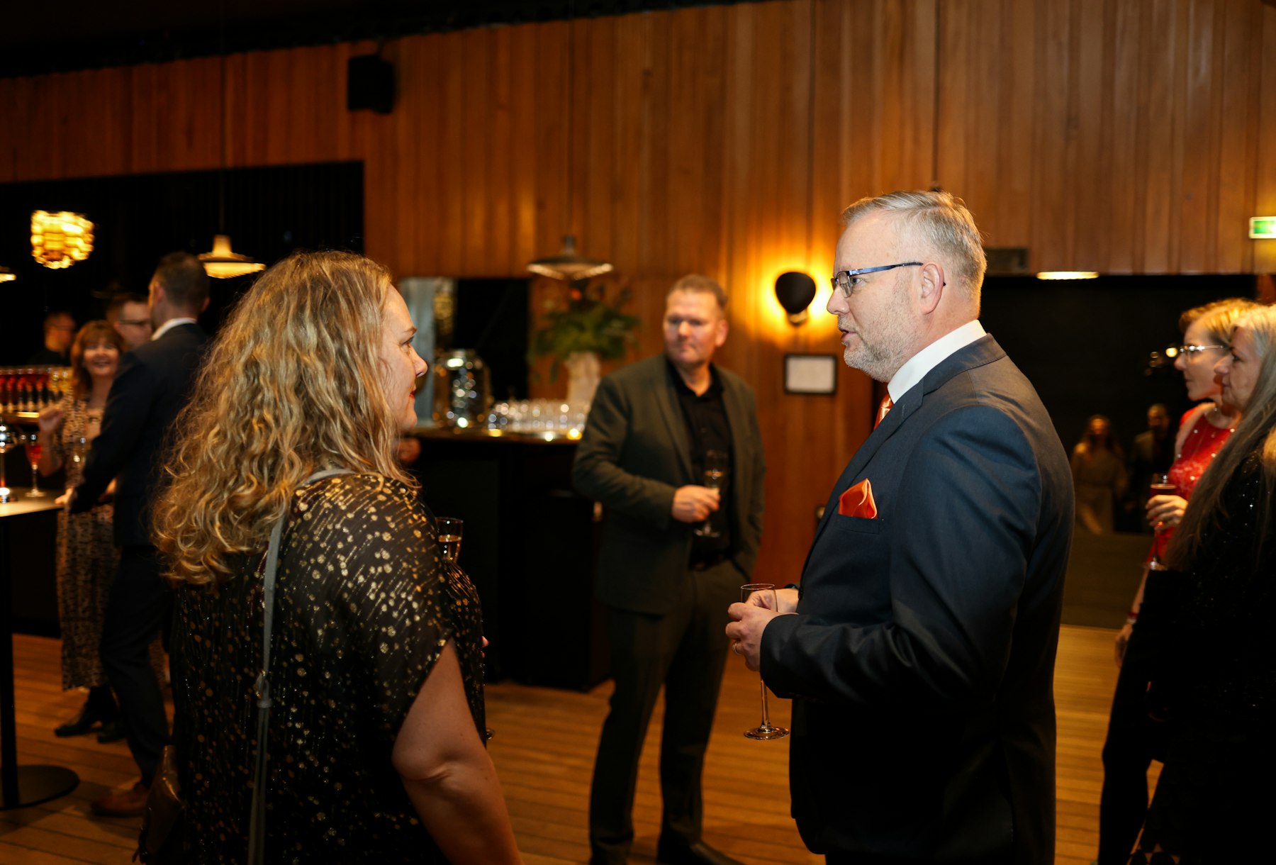 People gathered with drinks at a warm, candlelit business event, mid-conversation.
