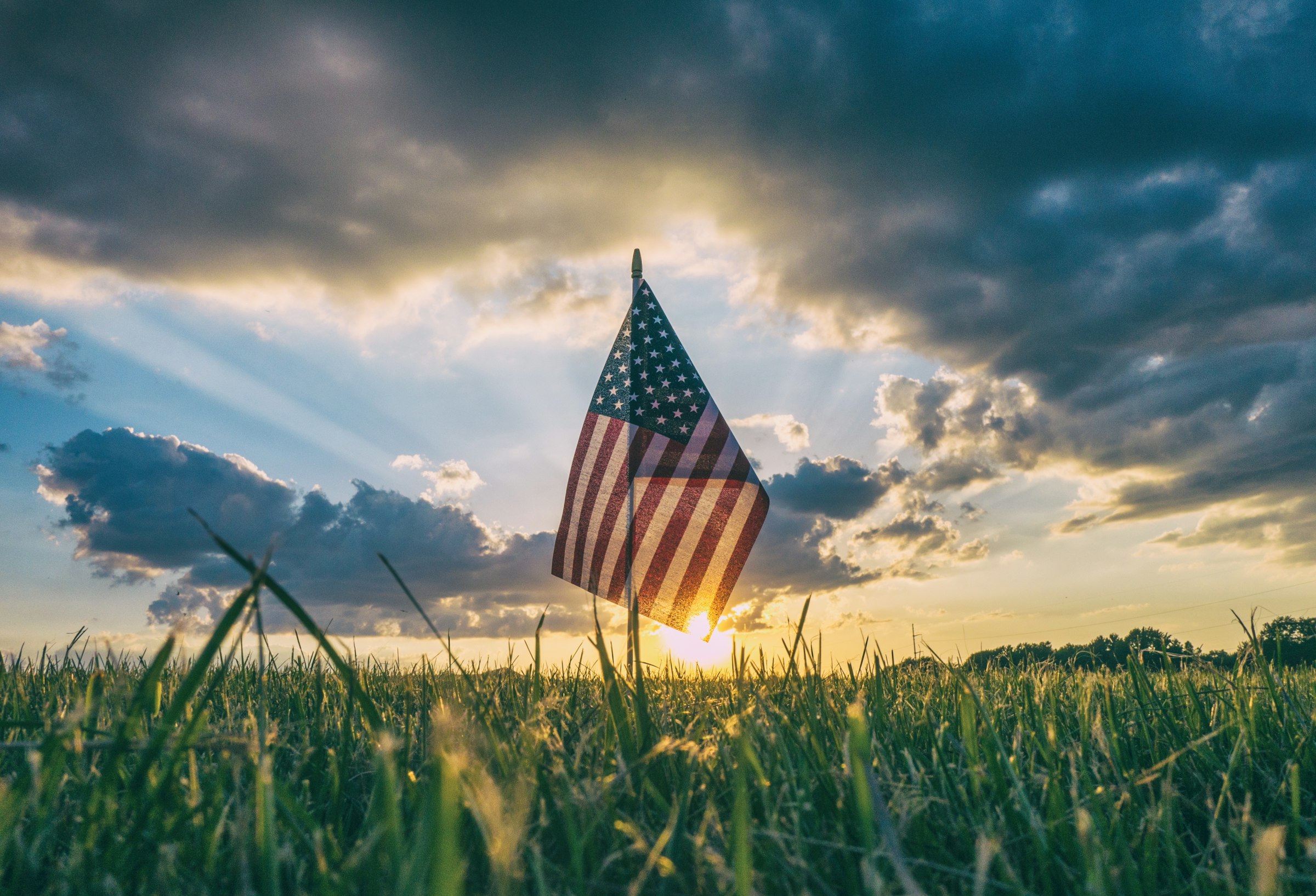 An American flag set on a grass field, the kind placed at cemeteries on Memorial Day.