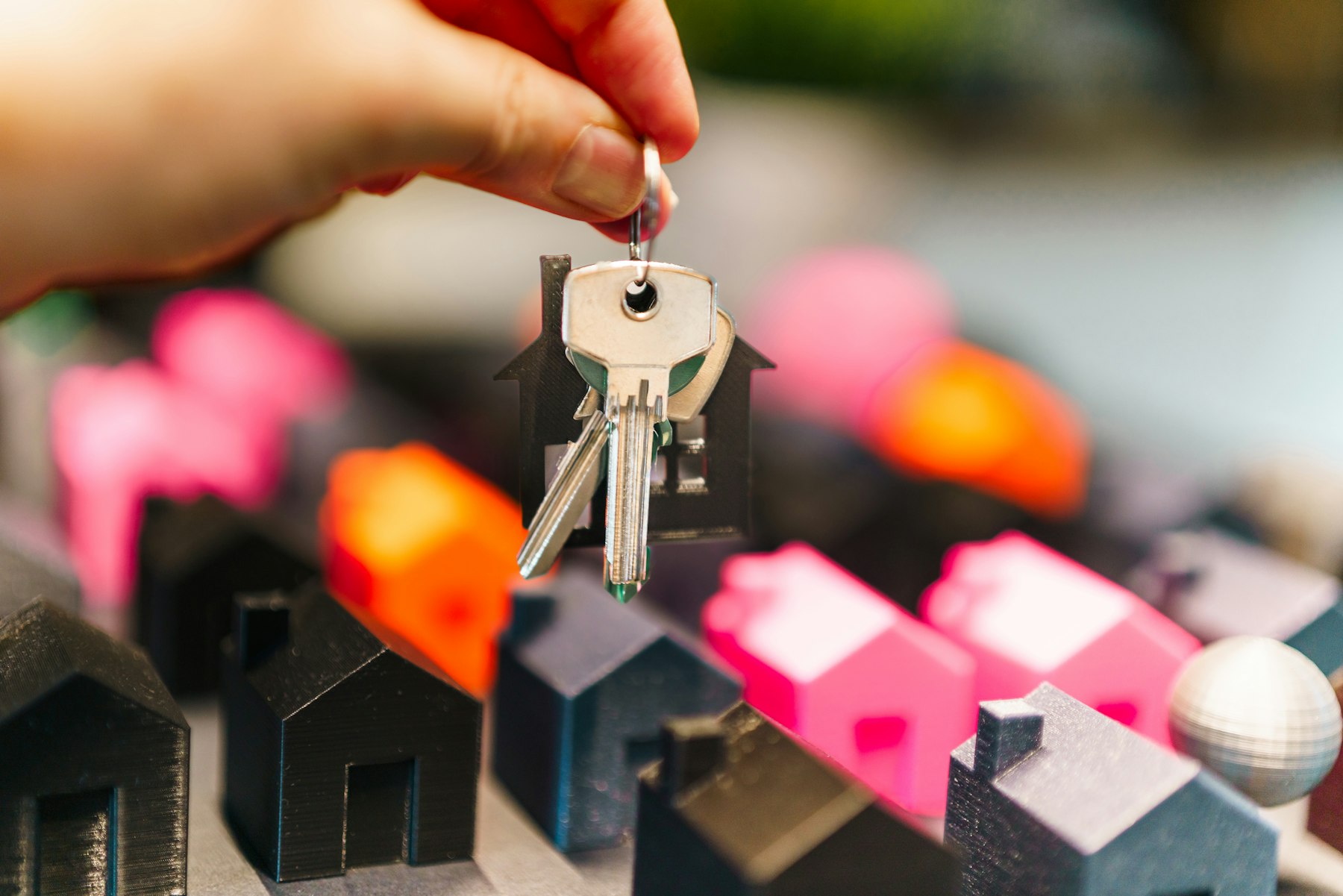 Hand holding house keys above a row of model homes